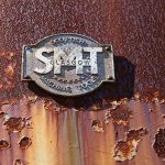 Close-up of a rusty metal plaque with smt glasgow inscription.